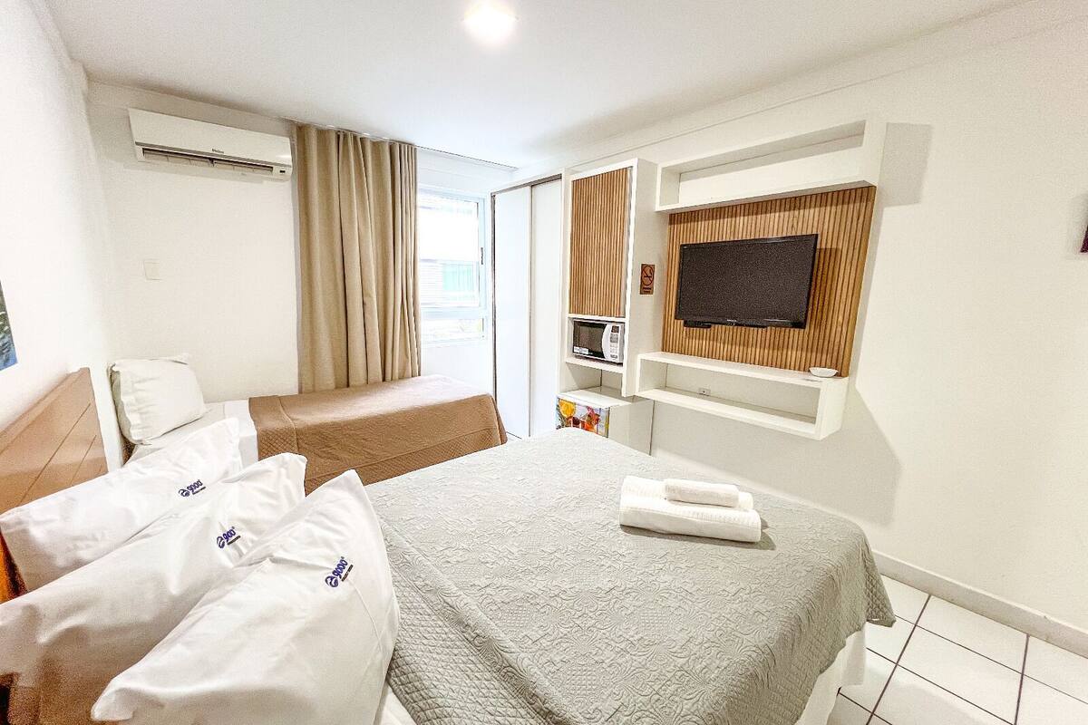 Ein Hotelzimmer mit zwei Betten, einem Fernseher, einer Mikrowelle und einem fensterbepflanzten Fenster.