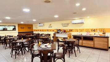 Um restaurante com várias mesas e cadeiras, um balcão de buffet e uma parede com um mural.