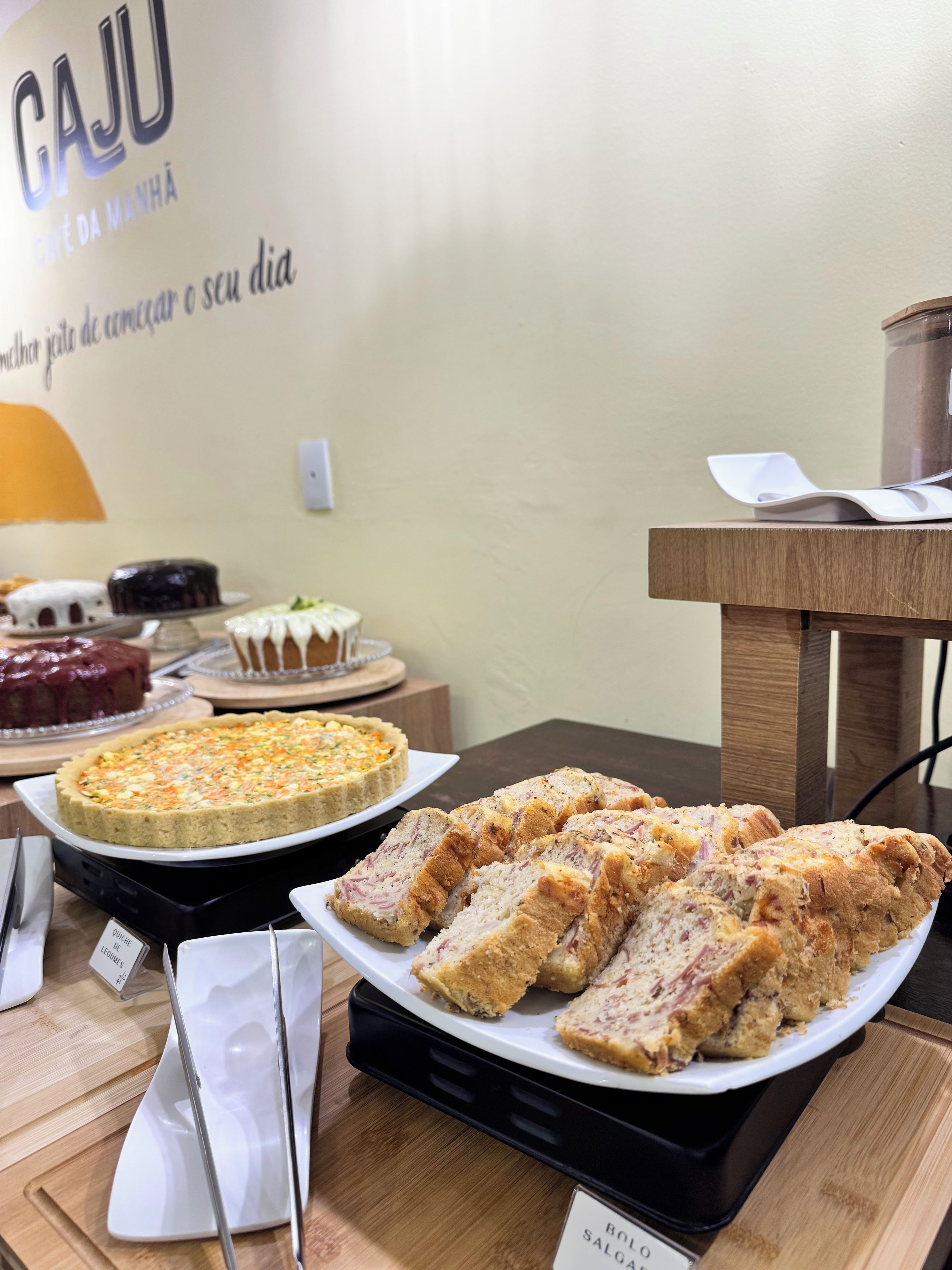 Uma mesa de buffet com diversos alimentos, incluindo uma quiche, um bolo e pão fatiado.
