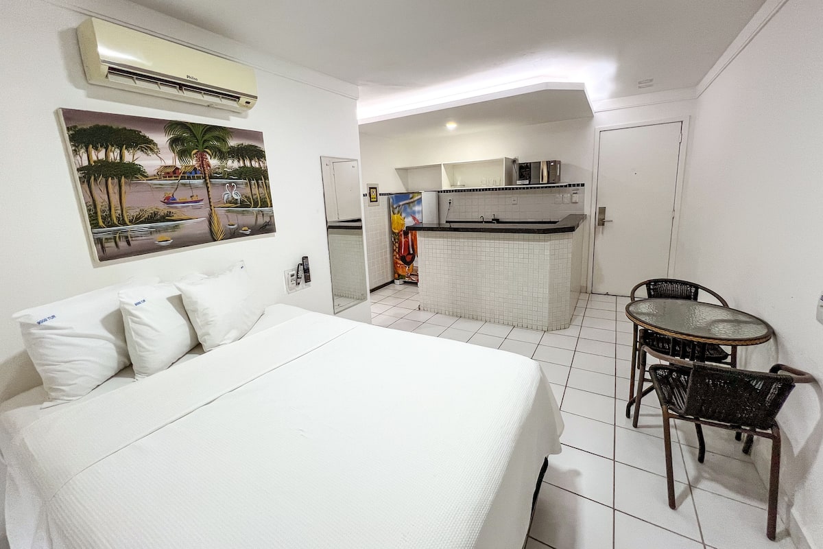 Ein Hotelzimmer mit Bett, einem kleinen Esstisch mit Stühlen, einer Küchenzeile und einem Bild an der Wand.