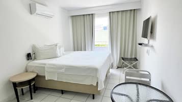 Quarto de hotel com cama, mesa pequena, cadeira, televisão e janela com cortinas.