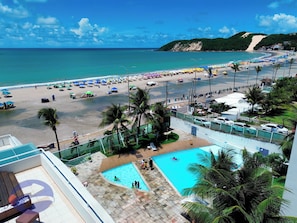A beach resort with a swimming pool, beach umbrellas, and palm trees.