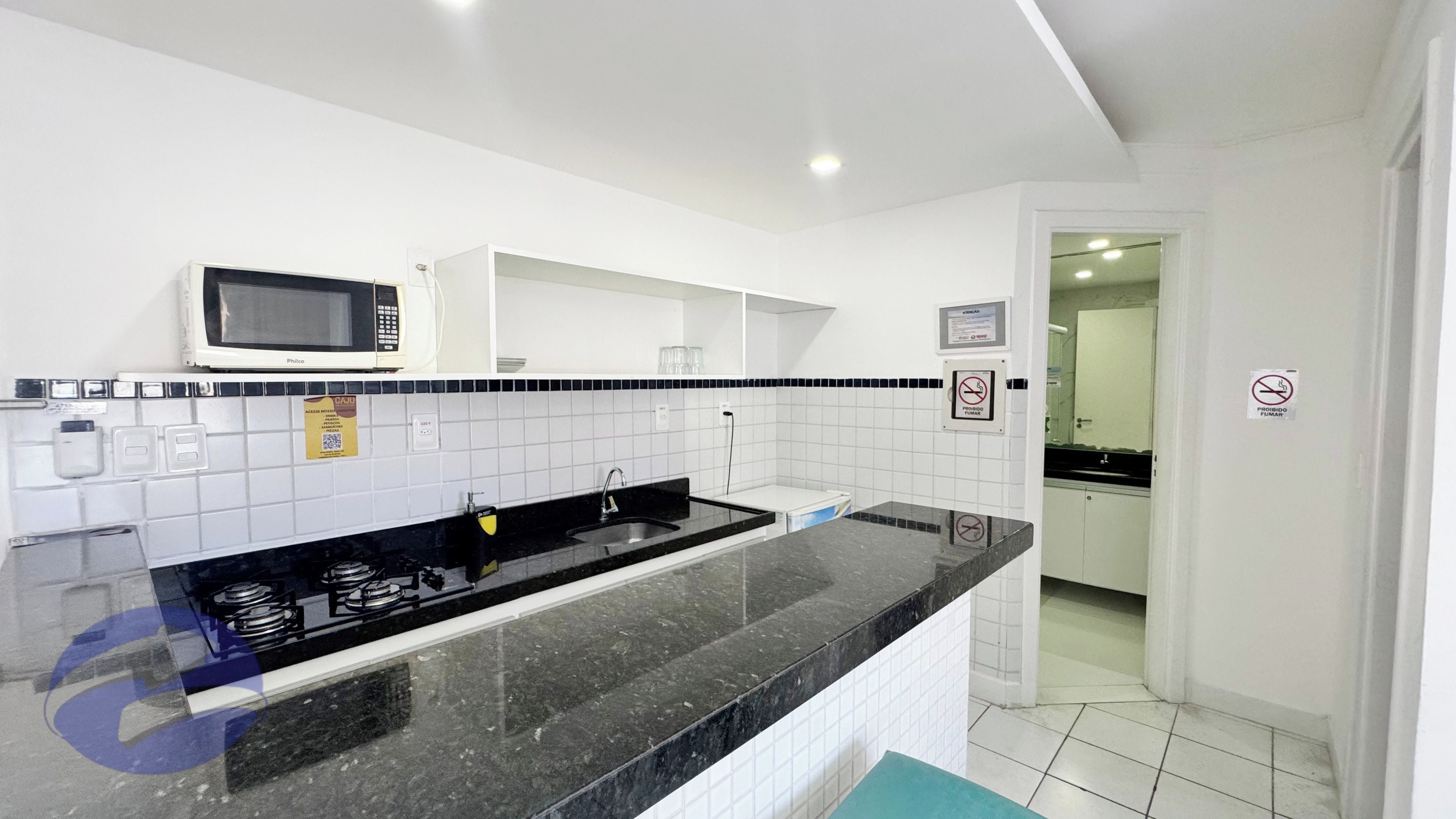 Cozinha moderna com bancada preta, armários brancos e micro-ondas.