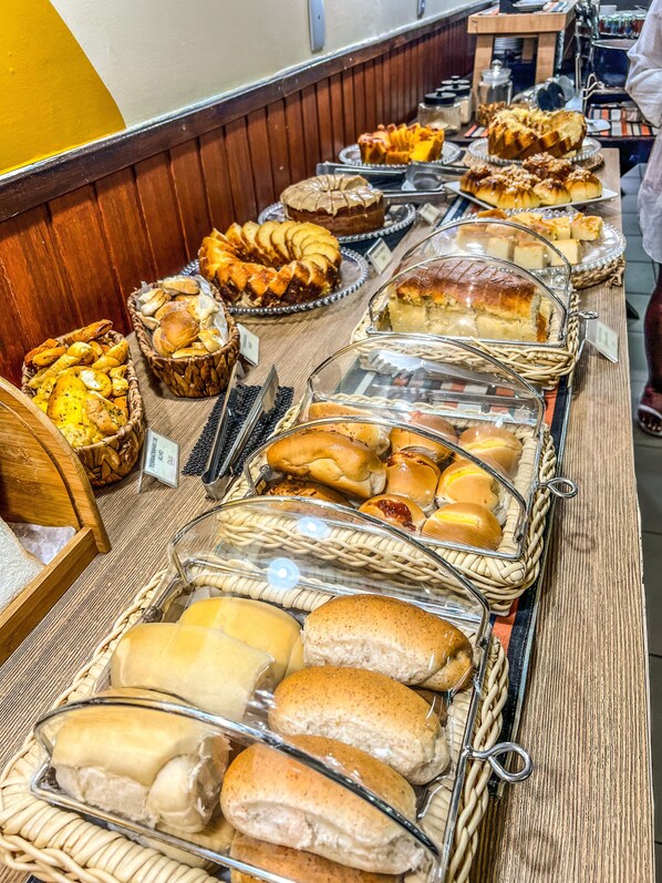 A buffet with various baked goods including bread, pastries, and cakes displayed in baskets and glass containers. -  Ponta Negra Beira Mar - Pimentel (Natal)