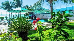 A pool area with umbrellas, palm trees, and a view of the ocean. -  Ponta Negra Beira Mar - Pimentel (Natal)