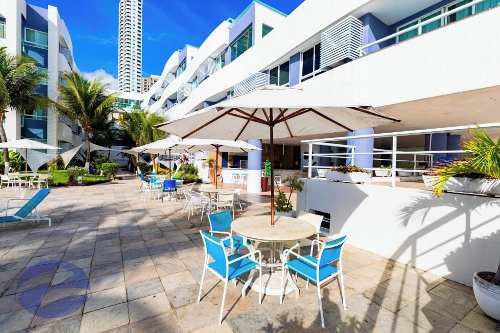 Pátio de hotel com área de estar externa, palmeiras e um edifício moderno ao fundo.