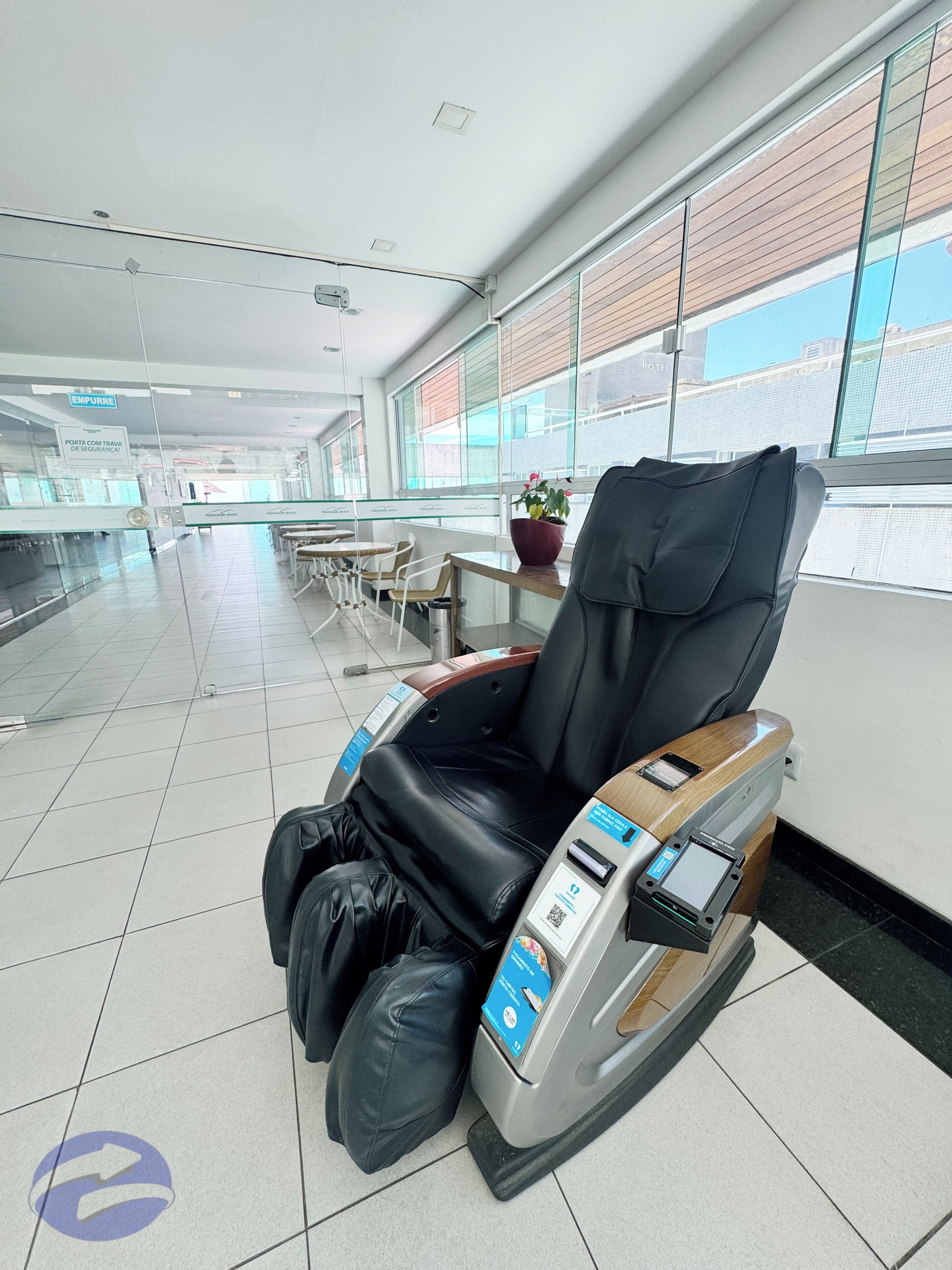 A massage chair in a hotel lobby with a tiled floor and large windows.