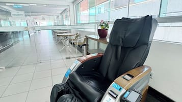 Uma cadeira de massagem em um saguão de hotel, com piso de azulejos e janelas amplas.