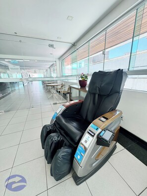 A massage chair in a hotel lobby with a tiled floor and large windows.