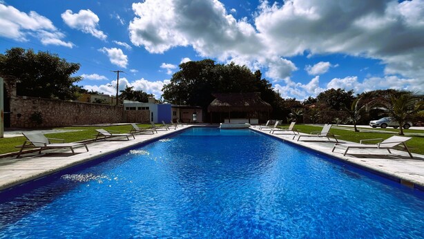 A swimming pool with lounge chairs, a thatched-roof structure, and a stone wall. - Casa Muranta (Cancún)