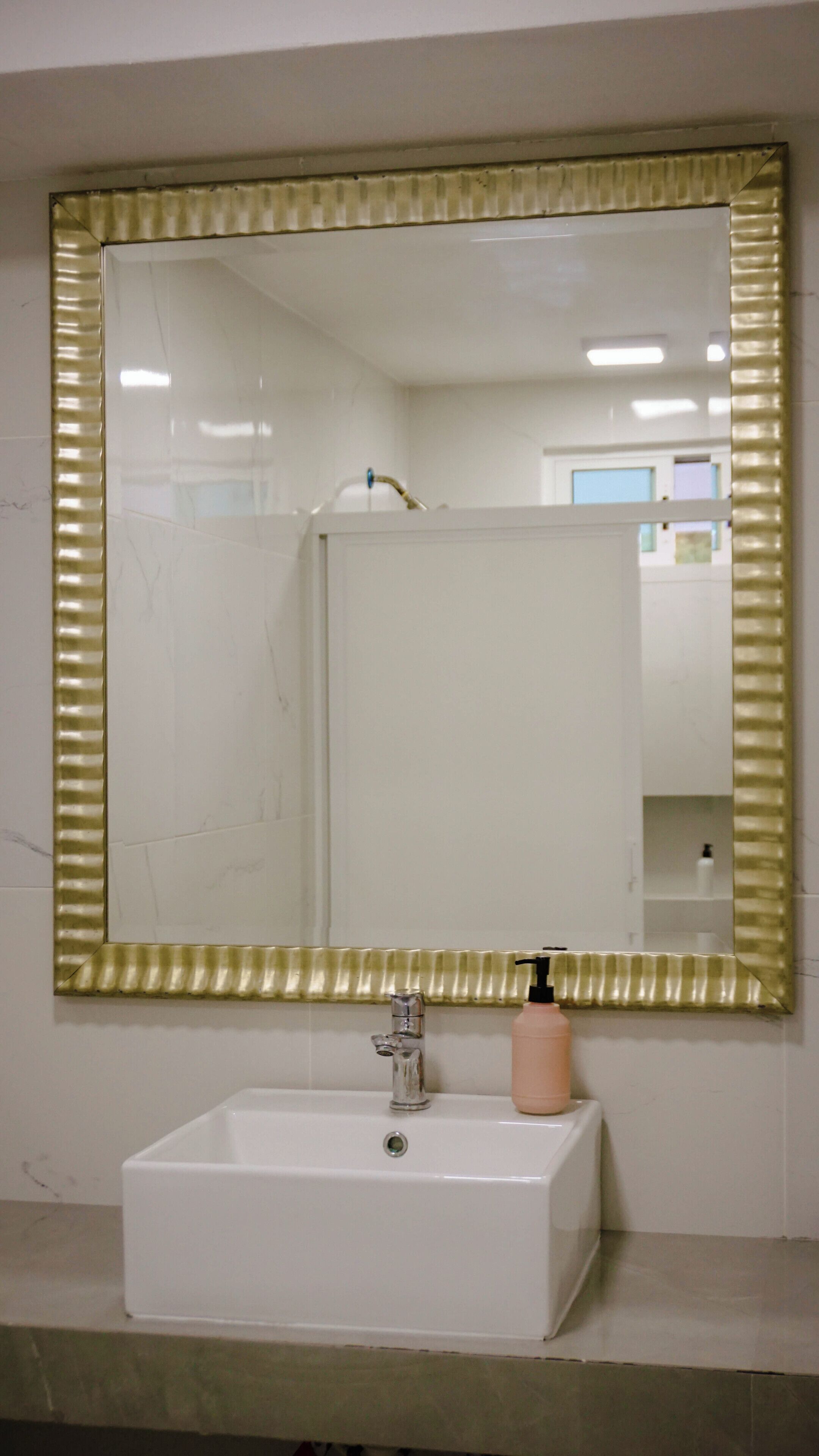 Une salle de bain avec un miroir rectangulaire, un lavabo blanc et un flacon de savon.