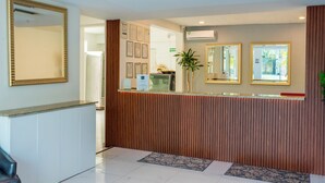 A reception area with a counter, wooden paneling, a large mirror, framed certificates, and an air conditioning unit. - Casa Muranta (Cancún)