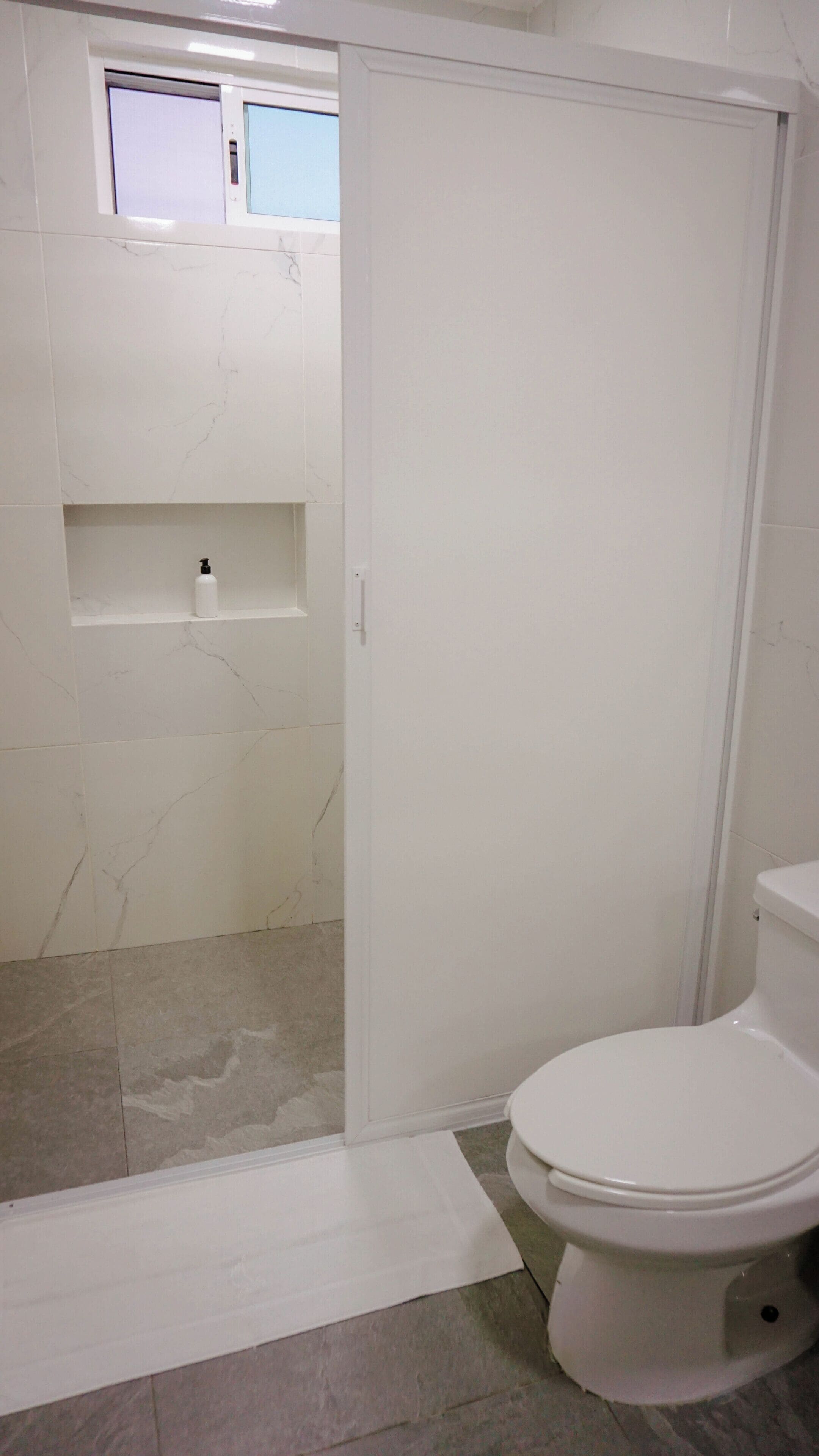 Un baño con inodoro, zona de ducha y un ventanal pequeño.