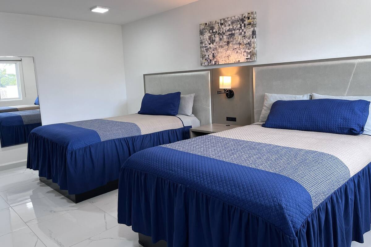 A hotel room with two beds, each with a headboard, a nightstand, and a wall-mounted lamp.