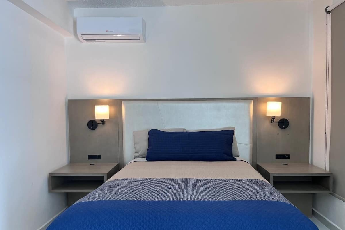 A hotel room with a bed, two bedside tables, and wall-mounted lamps.