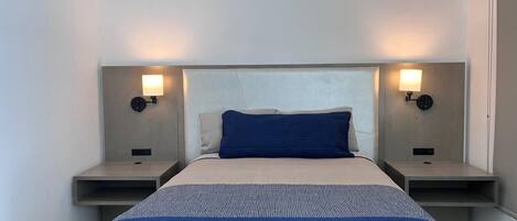 A hotel room with a bed, two bedside tables, and wall-mounted lamps.