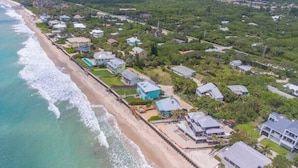 Vue aérienne d’une zone résidentielle côtière, avec des maisons, une plage et une vue dégagée sur l’océan.