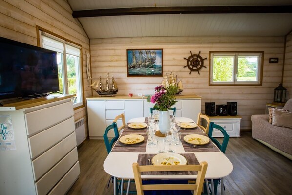 A cozy cabin interior with a dining table set for four, a ship model, and a ship wheel decoration on the wall.