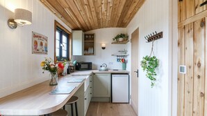 A compact kitchen with wooden ceiling beams, a small island with stools, a microwave, and a sink. - Woodpecker (Cambridge)