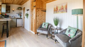 A cozy interior with a wooden ceiling, a dining area with a table and chairs, a sofa with floral cushions, and a painting of trees. - Woodpecker (Cambridge)