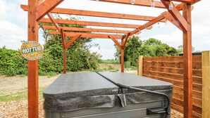 A hot tub under a wooden pergola with a sign that reads "WELCOME TO THE HOT TUB SIT BACK & RELAX." - Woodpecker (Cambridge)