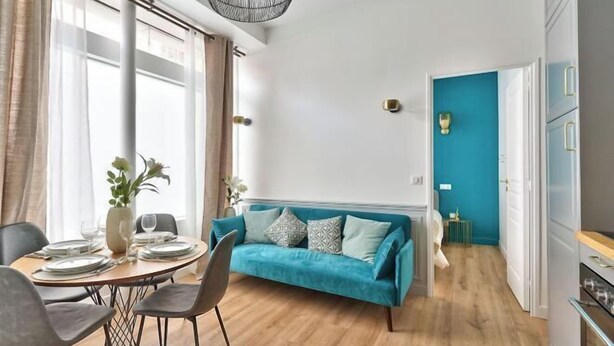 A modern living room with a teal sofa, wooden flooring, and a dining area with a table set for four. - Newly Renovated ! Stunning 2Br Apt in the Heart of Paris 15 (Paris)