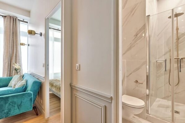 A modern bathroom with a glass-enclosed shower, a white toilet, and a blue sofa in the adjacent living area. - Newly Renovated ! Stunning 2Br Apt in the Heart of Paris 15 (Paris)