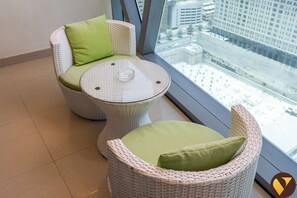 A wicker chair with a green cushion and a round table with a glass top, positioned by a window with a city view.