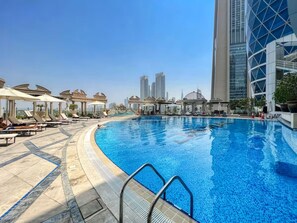 A swimming pool with lounge chairs and umbrellas, surrounded by modern buildings.