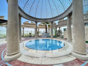 A circular pool with a clear blue center, surrounded by a tiled deck and supported by columns.