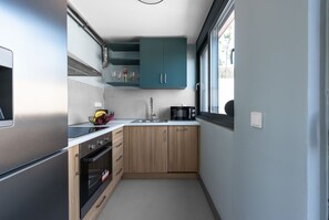 Compact kitchen with a stainless steel refrigerator, microwave, and sink, featuring light-colored cabinets and a window.