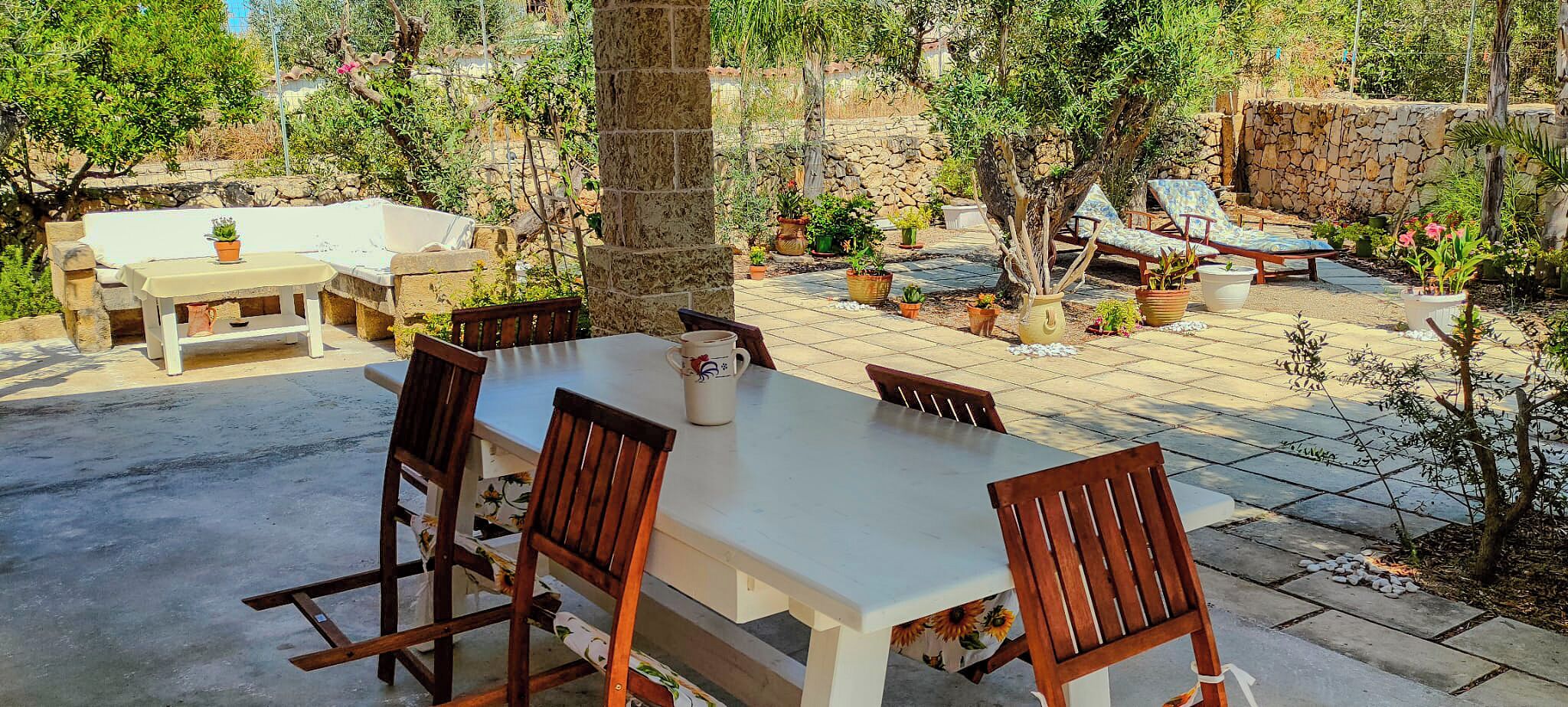 An outdoor patio with a table and chairs, surrounded by potted plants and a stone wall.