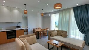 A modern living room with a sofa, a coffee table, a dining area with chairs, and a kitchen area with cabinets and a microwave. - Pinegrove Apartment (Durres)