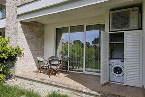 Un balcon équipé d’un lave-linge, d’une table avec des chaises et d’une grande porte-fenêtre coulissante.