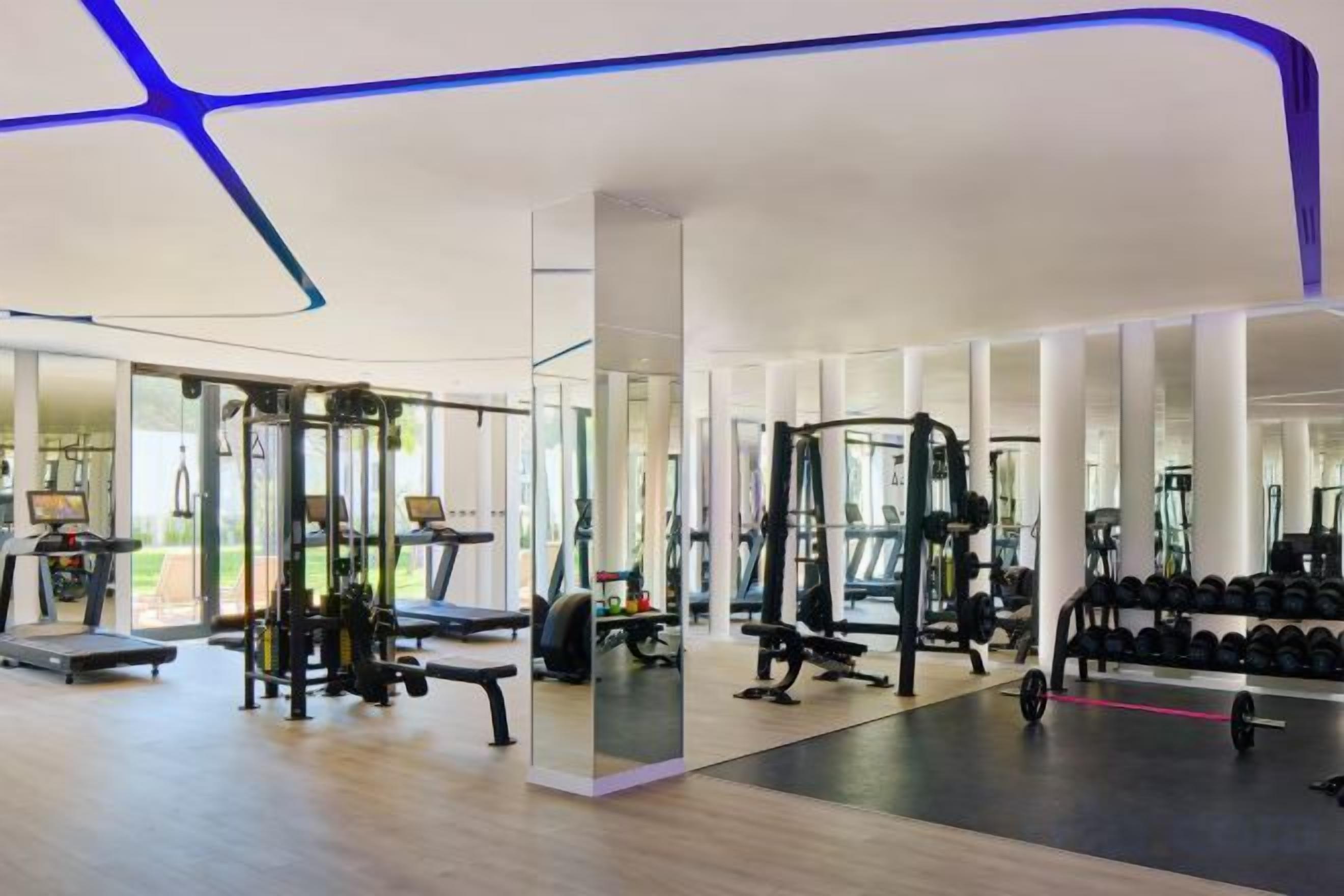 A modern gym with various exercise equipment, large windows, and a clean, open floor plan.