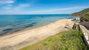 A beach with clear blue water, a sandy shore, and a small structure on the right.