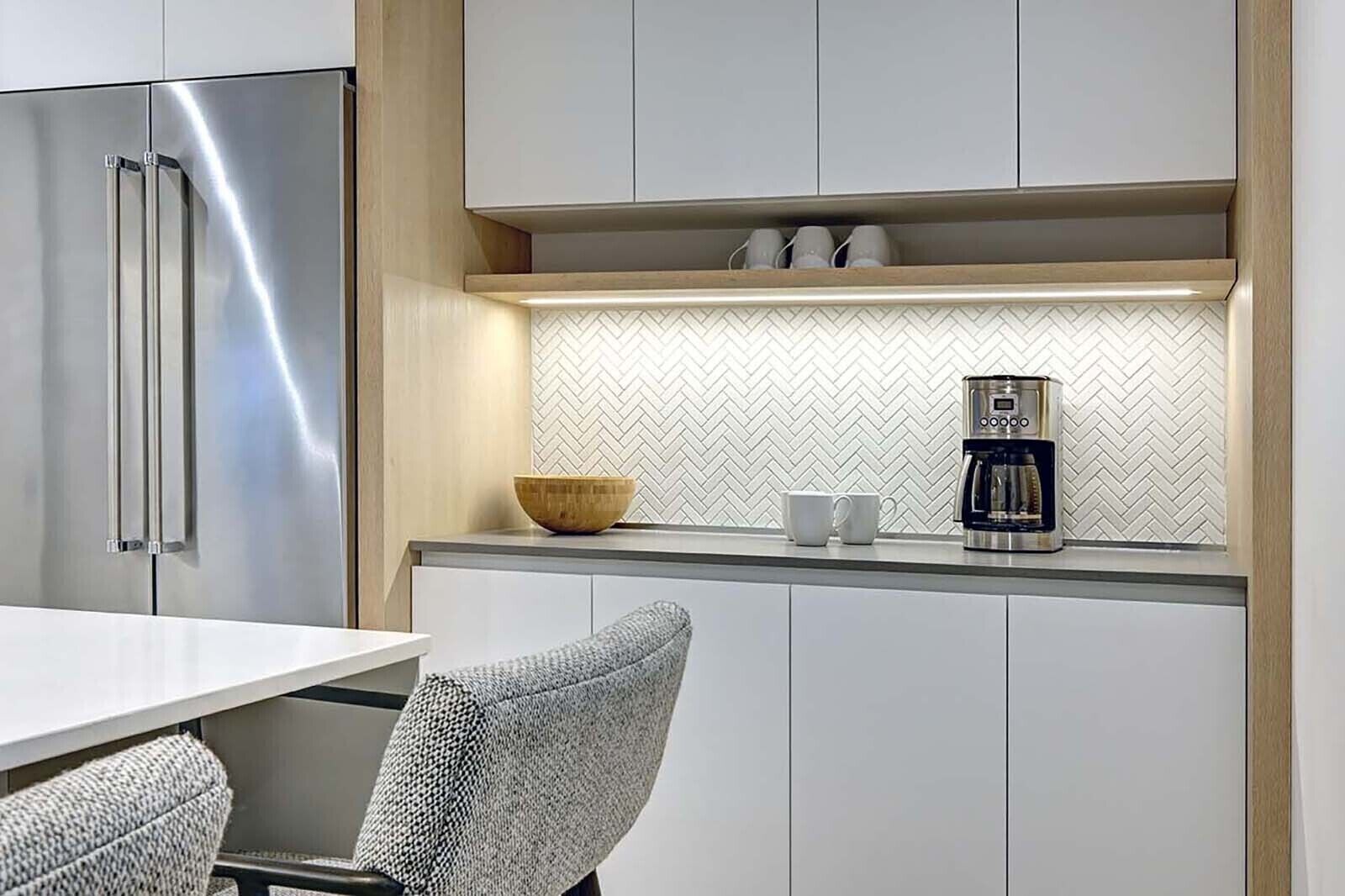 A modern kitchen with a stainless steel refrigerator, a coffee maker, and a herringbone-patterned backsplash.