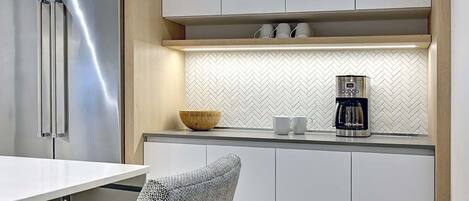 A modern kitchen with a stainless steel refrigerator, a coffee maker, and a herringbone-patterned backsplash.