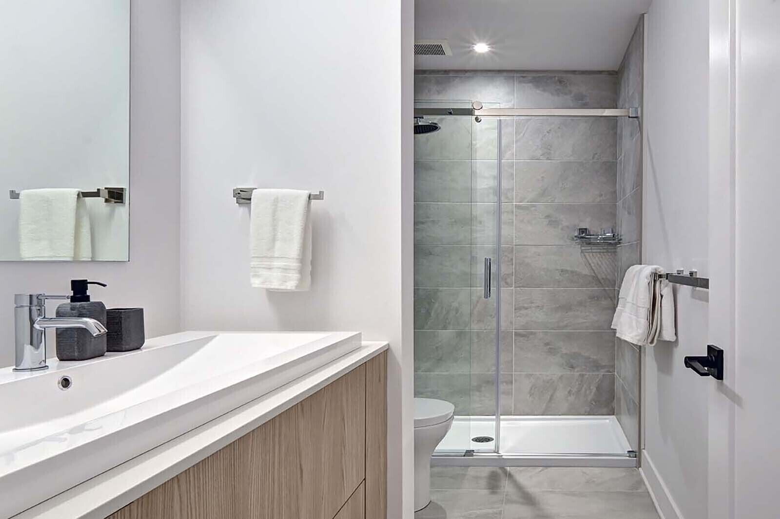A modern bathroom with a white vanity, a glass shower enclosure, and a toilet.