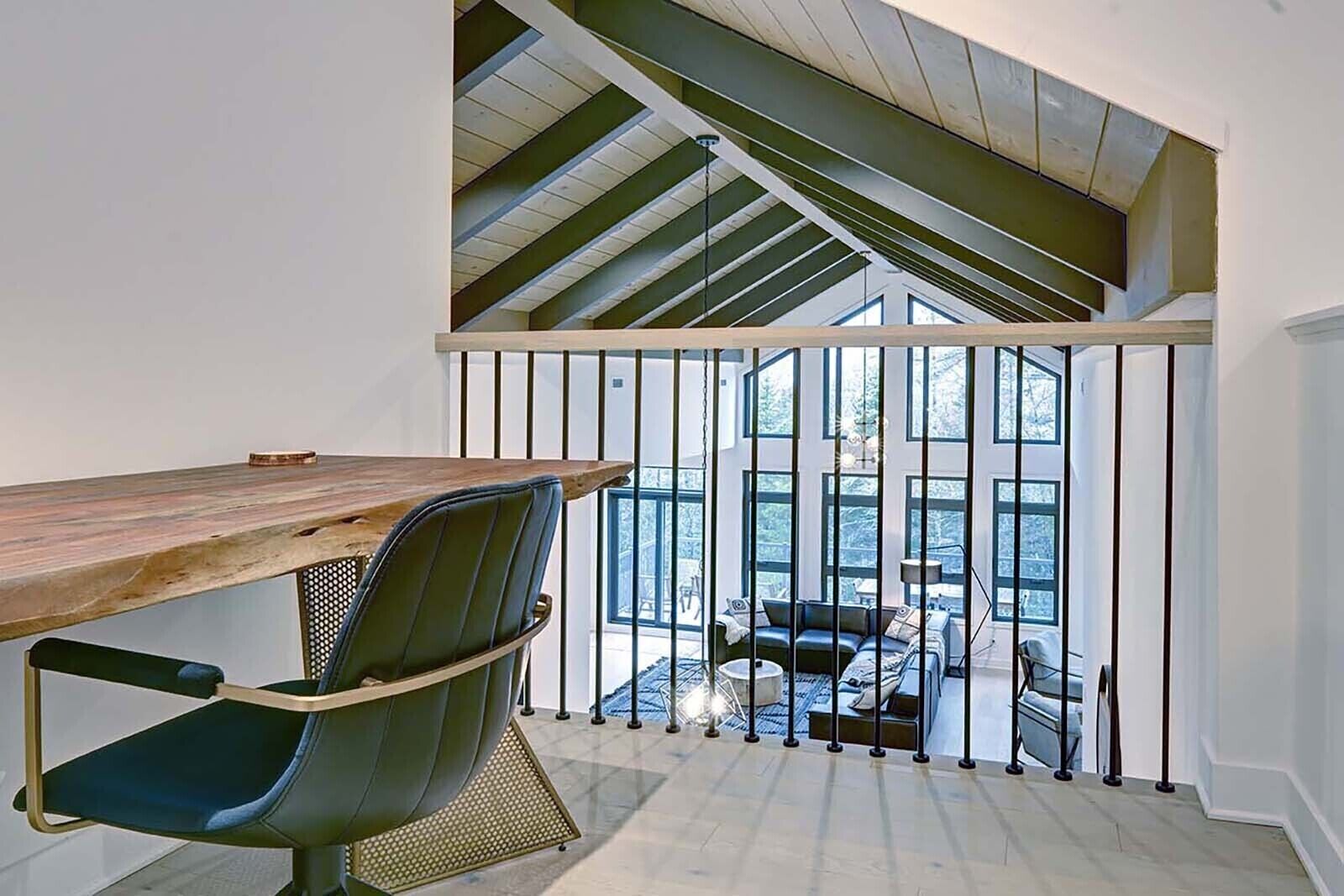 Ein modernes Loft-Zimmer mit großem Holztisch, bequemen Sessel und Blick auf einen Balkon mit Sitzgelegenheit.