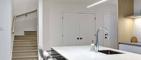 A modern kitchen with a central island, a built-in sink, and a staircase leading to another level.