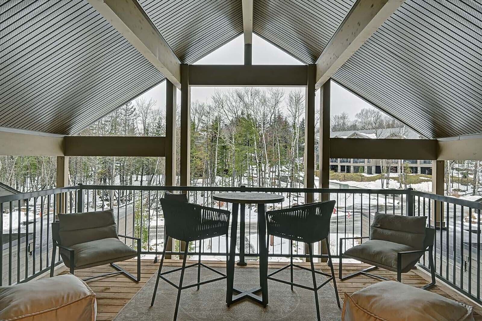 A covered outdoor seating area with a table and chairs, overlooking a snowy landscape.