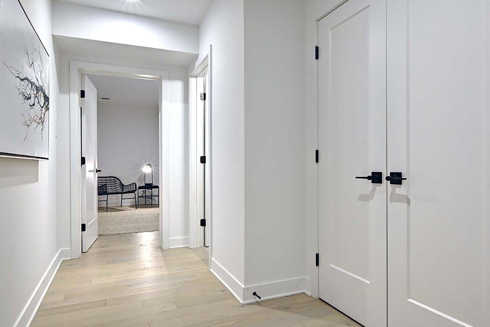 Un pasillo con paredes blancas y suelo de madera que conduce a una habitación con una cama y una lámpara.