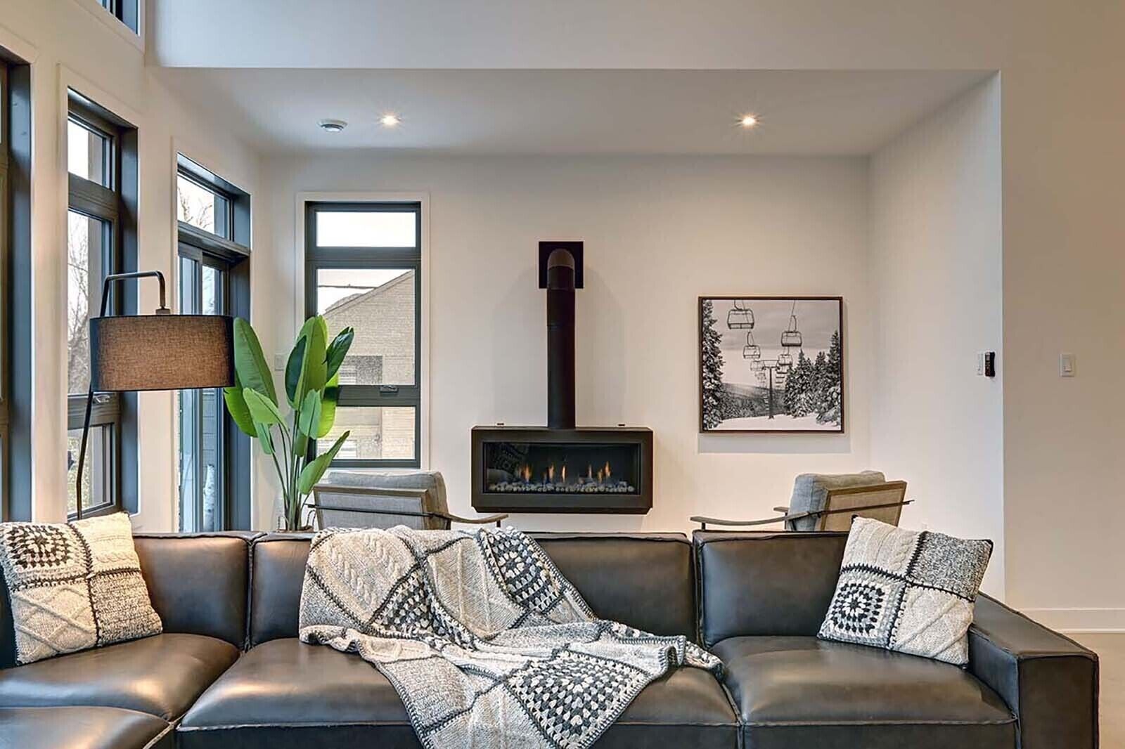 A living room with a fireplace, leather sofa, and a large window.