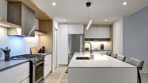 Et moderne køkken med en central ø, rustfrie hvidevarer og en backsplash i et fiskebensmønster.