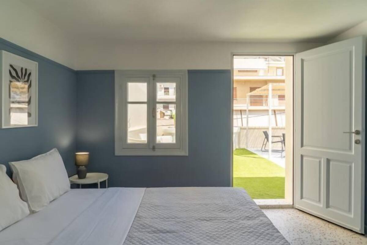 A bedroom with a bed, a nightstand, a window, and a door leading to an outdoor area.