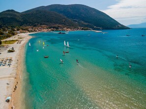 A coastal area with clear turquoise waters, a sandy beach, and a mountainous backdrop.