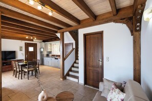 Amplia sala de estar con techo de madera, una mesa de comedor con sillas, un sofá y una cocina al fondo.