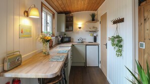 A compact kitchen with wooden ceiling, white walls, and a small dining area. - The Heron (Cambridge)