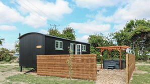 A small black cabin with a wooden fence, a pergola, and a hot tub. - The Heron (Cambridge)
